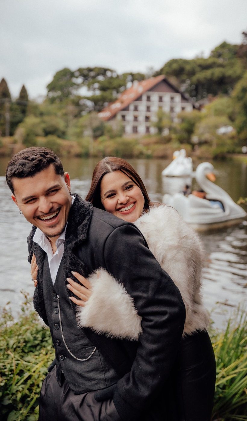 Rachel e Gabriel sorrindo abraçados, à beira do Lago Negro em Gramado, com os pedalinhos de cisne ao fundo